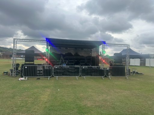 7X5 trailer stage with out riggers Outdoor stage setup with lighting and sound equipment in a grassy field.
