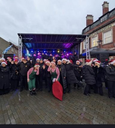 6X4.5 Trailer stage A group of carolers in festive attire poses in front of a stage during a Christmas event.