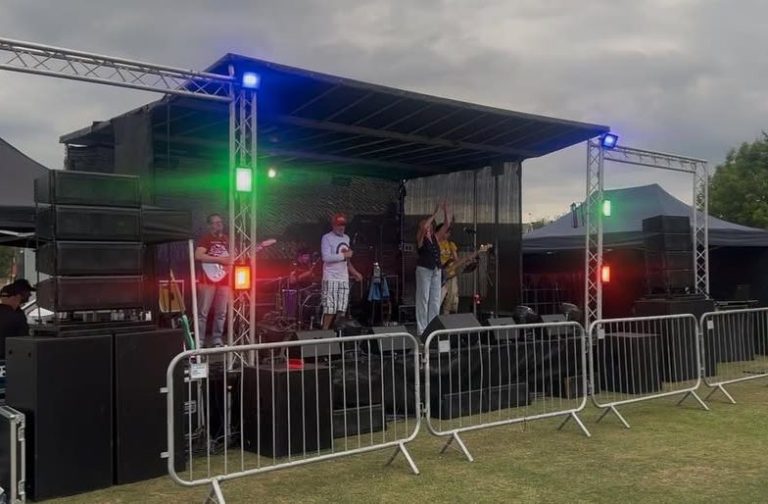 6X4 TRAILER STAGE A band performing on stage with colourful lights in an outdoor setting.
