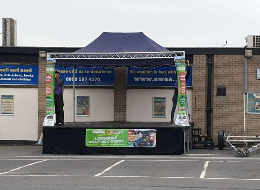 pop up stage 4.5x3 mtr Stage setup with a blue canopy and promotional banners in an empty parking lot.