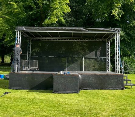 6x4 truss build stage A raised outdoor stage setup with black framework and grass surroundings.